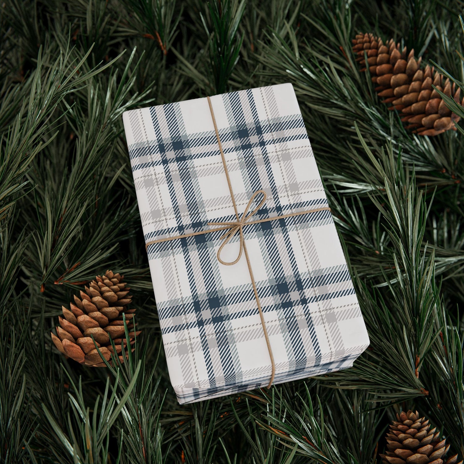 Plaid fabric roll tied with twine on a bed of pine needles and pine cones