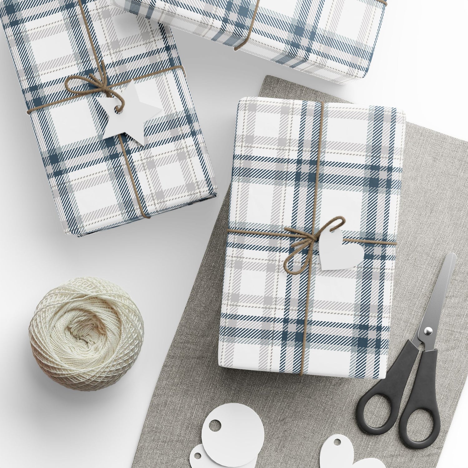 Plaid-patterned gift boxes with string, scissors, and yarn on a white surface