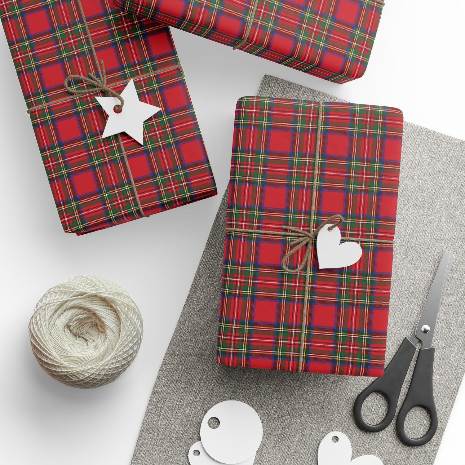 Red plaid gift wrap with a heart tag, scissors, and yarn on a white surface
