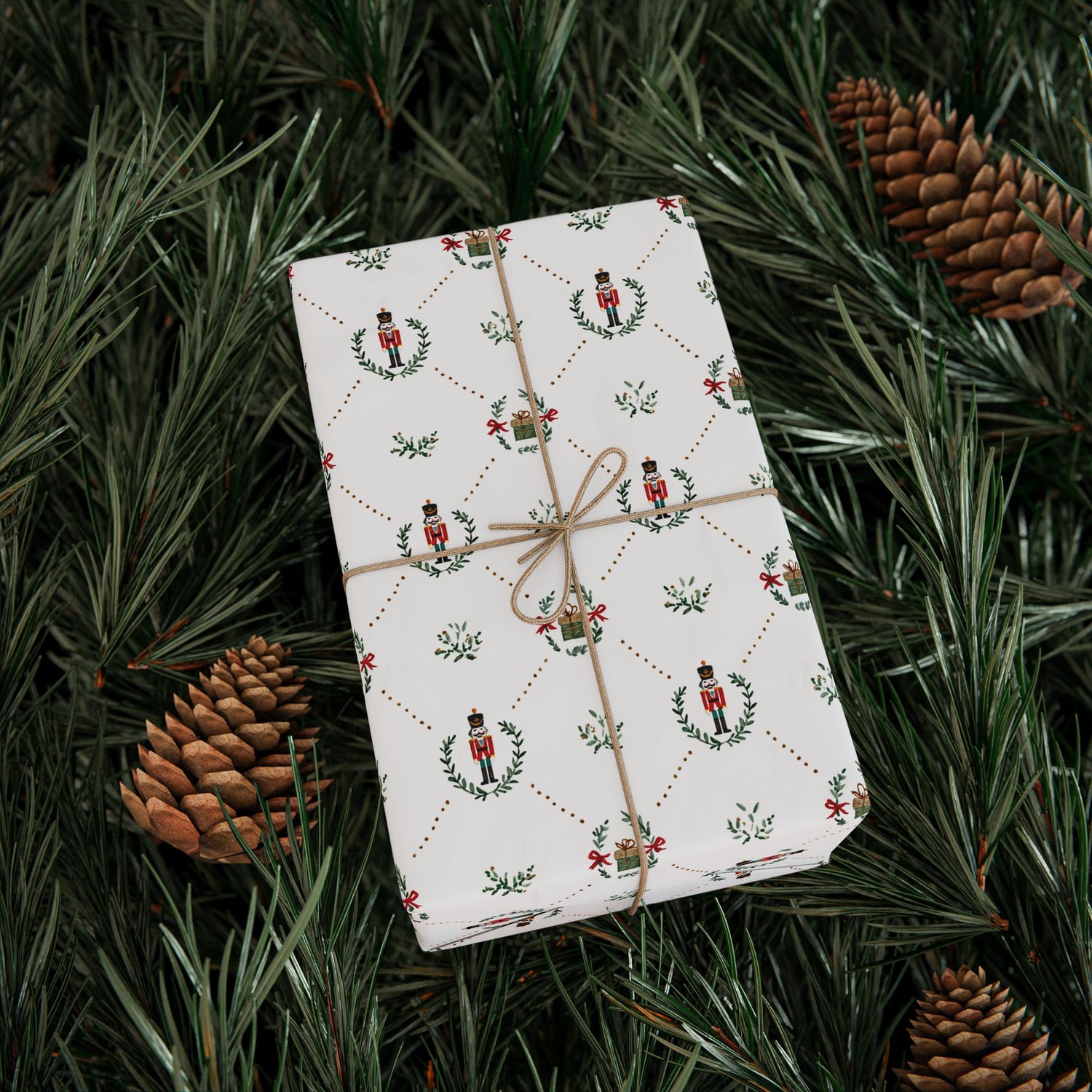 Gift wrapped in festive paper with nutcrackers and wreaths, tied with brown string, on a bed of pine needles and pine cones.