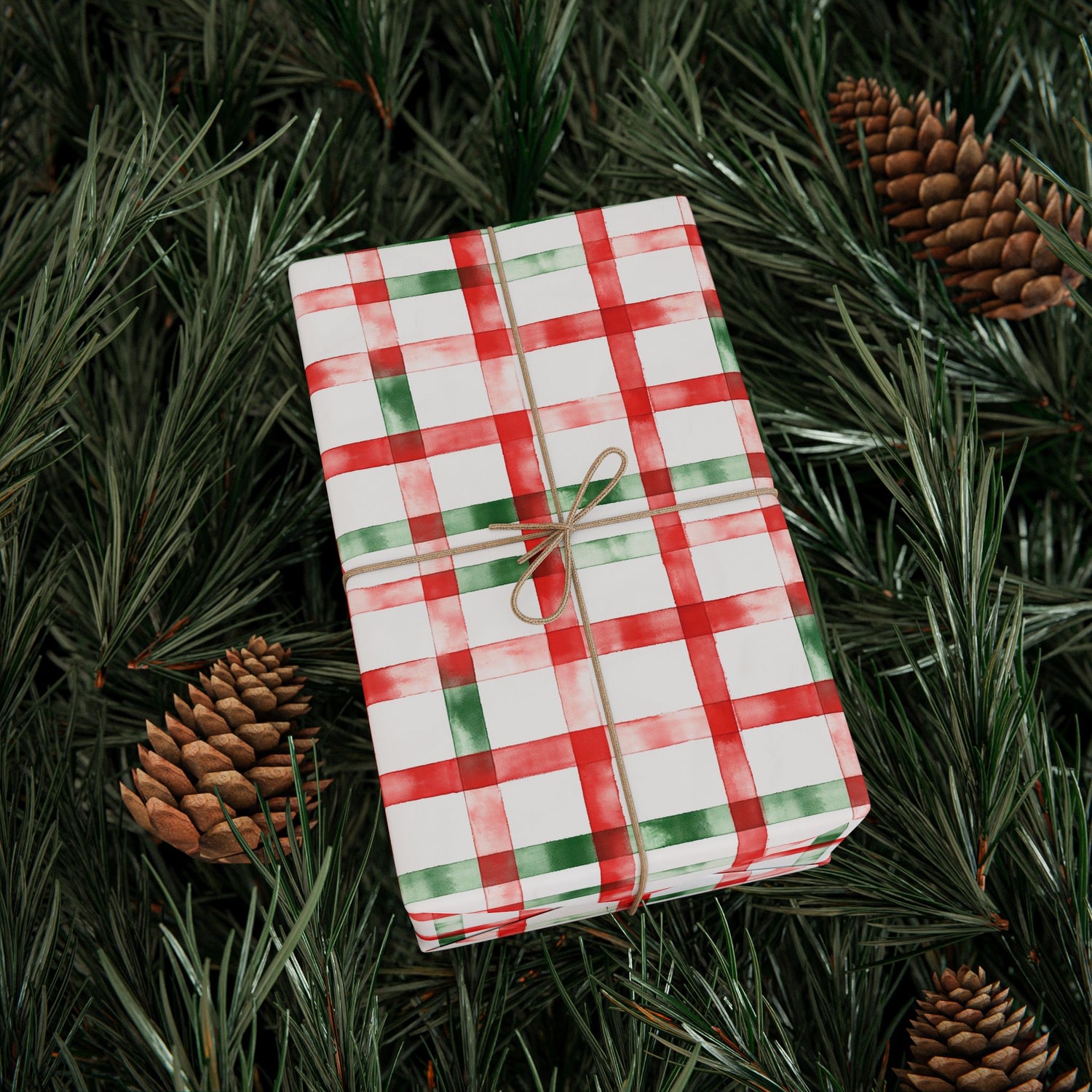 Gift wrapped in red and green checkered paper with a brown ribbon on pine branches.