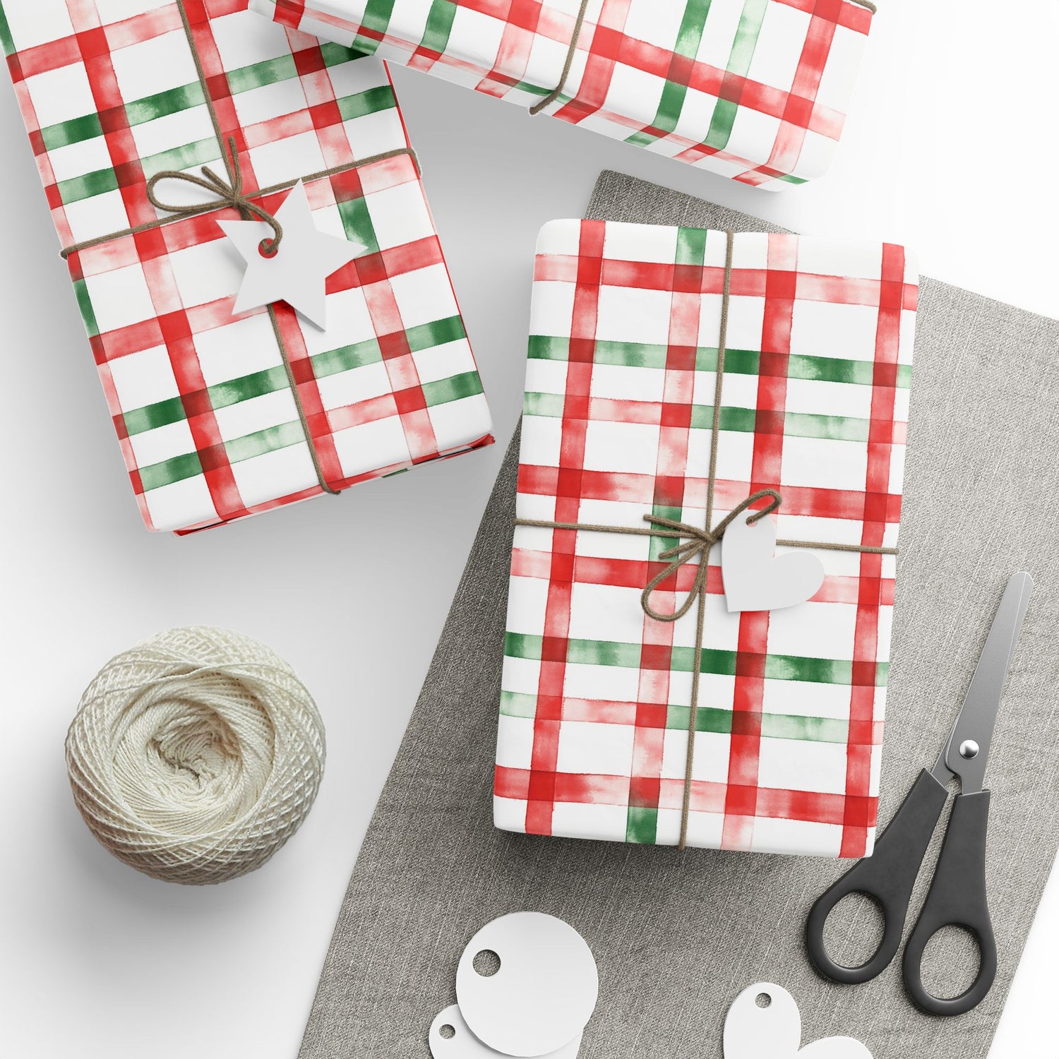 Gifts wrapped in red and green plaid paper with scissors and twine on a white surface