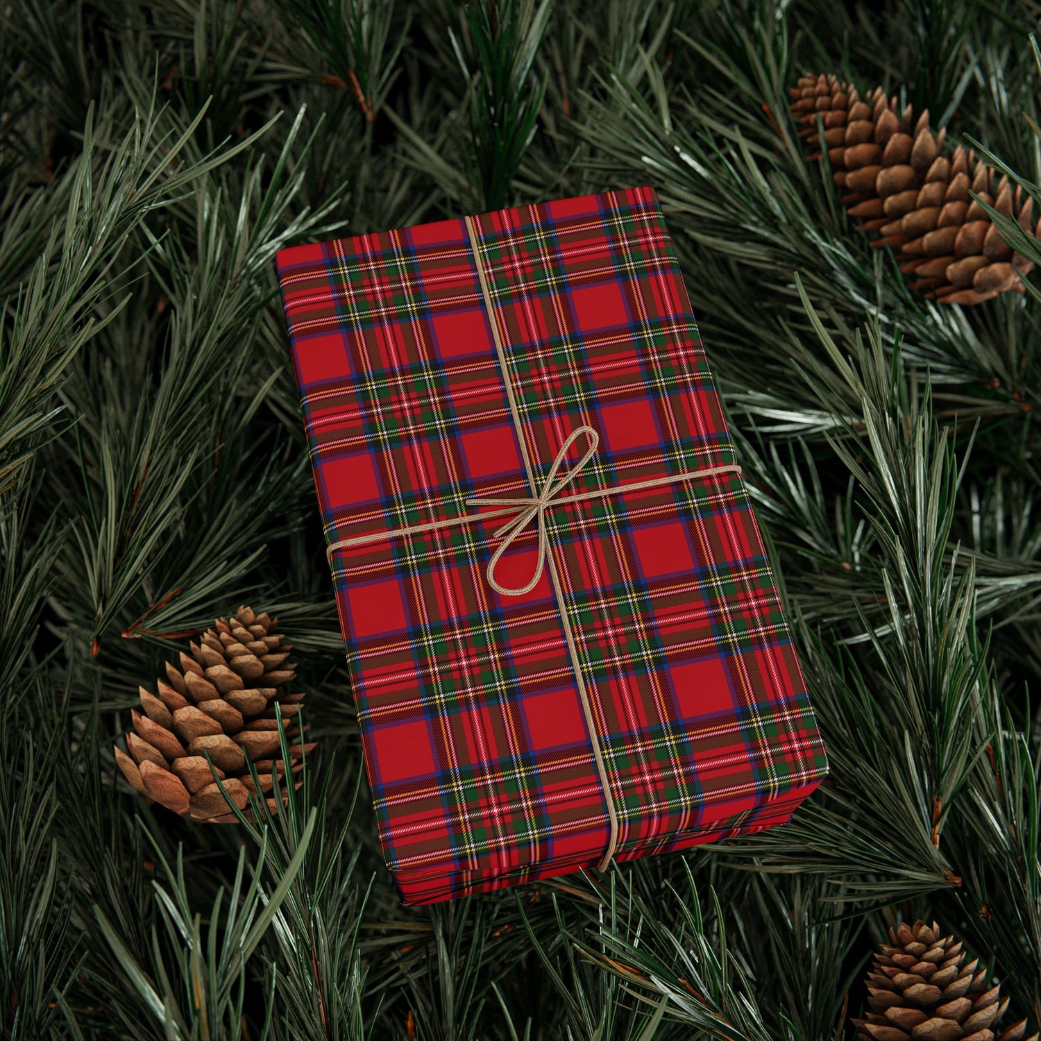 Red plaid fabric with a string bow on green foliage with pine cones