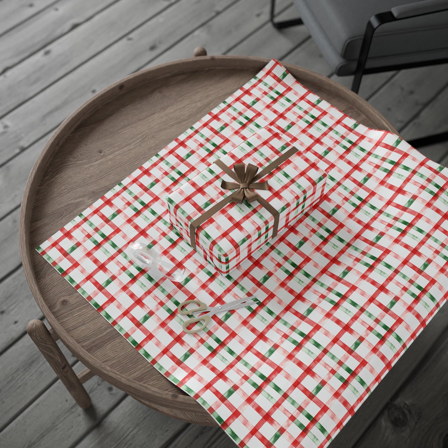 Gift box with a bow on a red and green checkered tablecloth on a wooden tray.